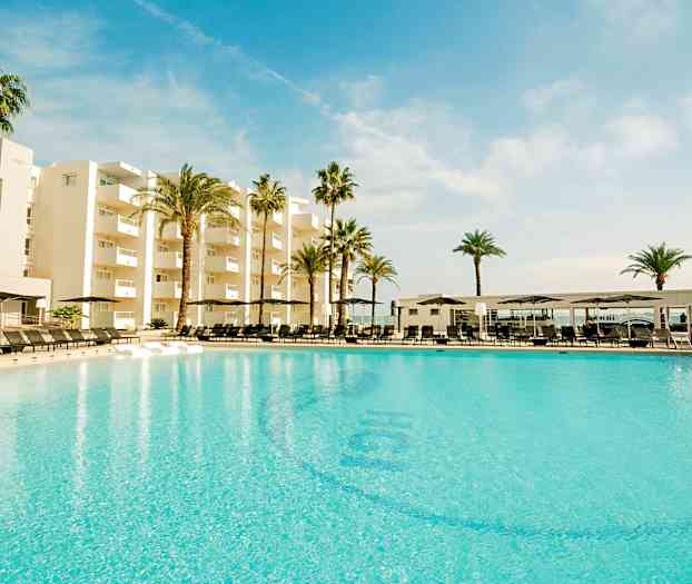 En stor pool foran et moderne hotel omgivet af palmer under en blå himmel. (AI-genereret tekst)