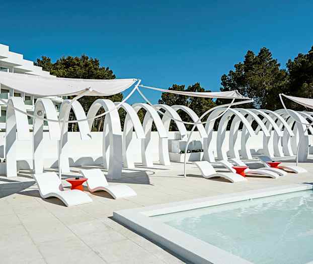 Hvid arkitektur med buer, samt liggestole og røde borde ved en pool. (AI-genereret tekst)