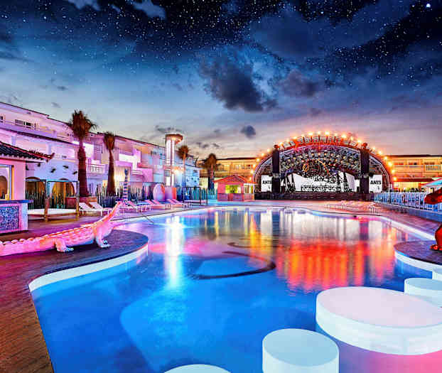 En udendørs pool ved et oplyst hotelområde under nattehimlen. (AI-genereret tekst)