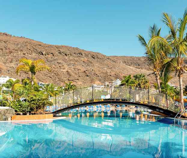 En pool med en bro og palmer omgivet af bjerge. (AI-genereret tekst)