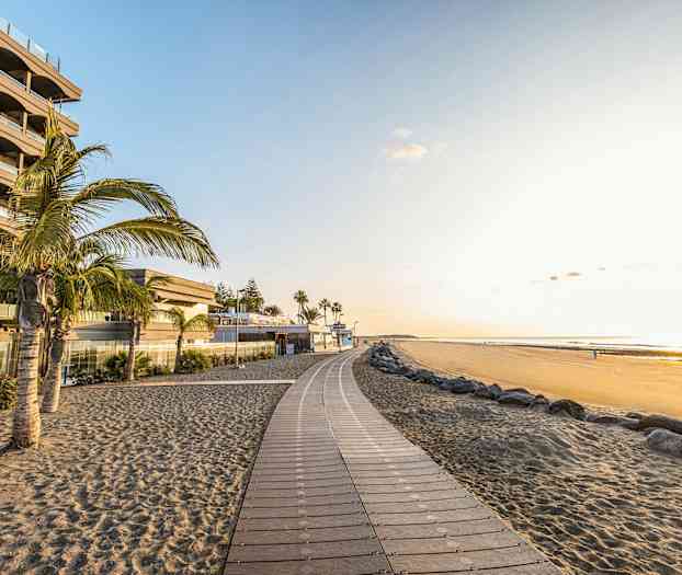 En strandpromenade ved en sandstrand med palmer og bygninger. (AI-genereret tekst)