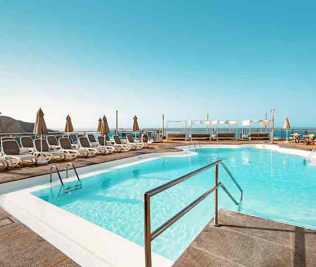 Poolområde med liggestole og parasoller samt udsigt over havet. (AI-genereret tekst)