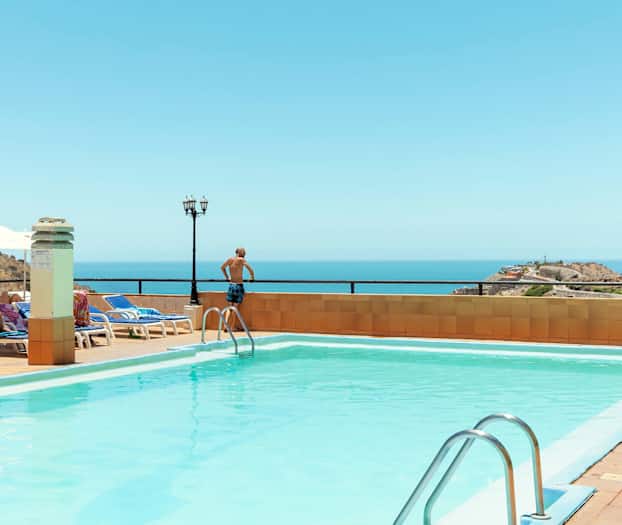 Udendørs pool med havudsigt, liggestole og parasoller. (AI-genereret tekst)