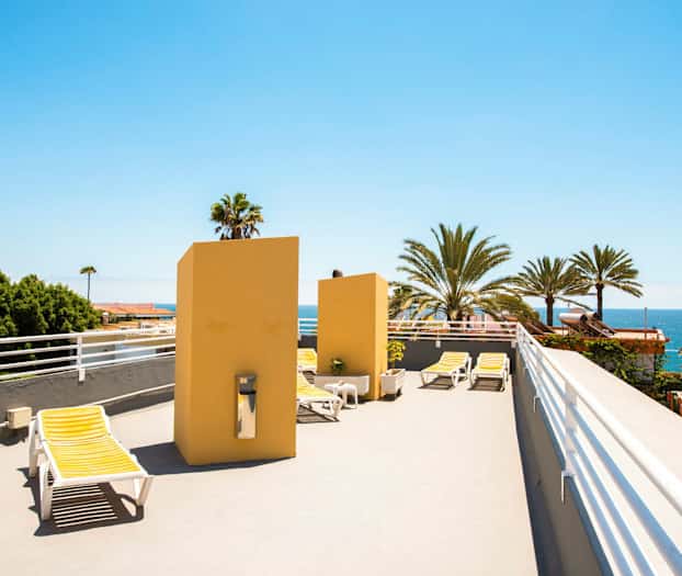 En tagterrasse med liggestole og udsigt over palmer og havet. (AI-genereret tekst)