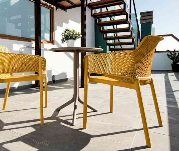 To gule stole og et bord på en solrig terrasse med trapper og plante. (AI-genereret tekst)