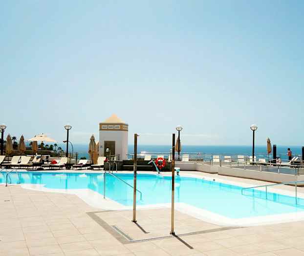 Udendørspool med liggestole og udsigt over havet. (AI-genereret tekst)