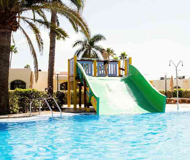 En vandrutsjebane ved en pool, omgivet af palmer og bygninger. (AI-genereret tekst)