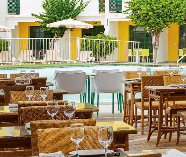 Udendørsservering med flettede stole og glasborde ved en pool. (AI-genereret tekst)