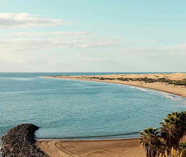 Udsigt over en strand med sandklitter, havet og en smal stenmole. (AI-genereret tekst)
