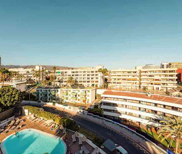 Udsigt over et hotelområde med pool, omgivet af bygninger under en klar himmel. (AI-genereret tekst)