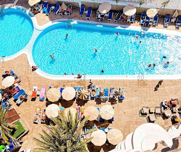 En udendørs swimmingpool med liggestole og parasoller ved siden af. (AI-genereret tekst)