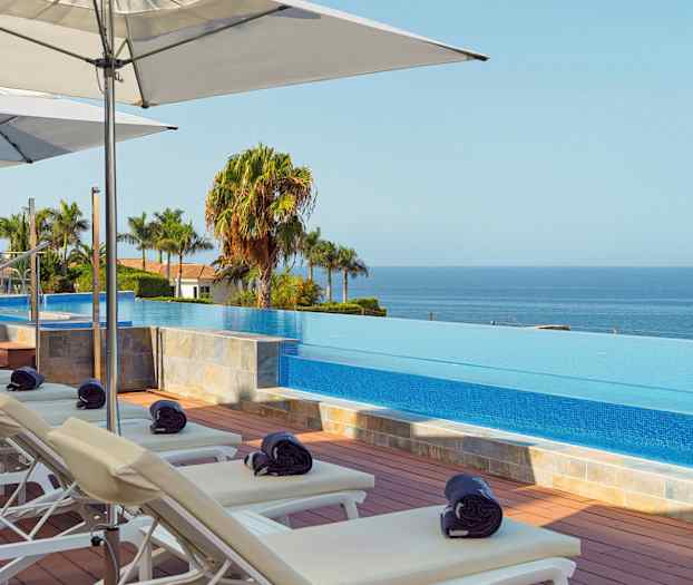 Liggestole og parasoller ved en infinity-pool med udsigt over havet. (AI-genereret tekst)