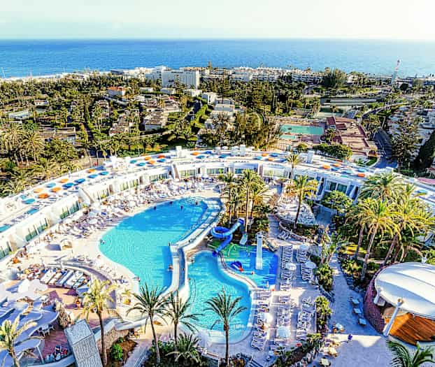 Luftfoto af et stort resort med poolområde og omgivet af palmer. (AI-genereret tekst)