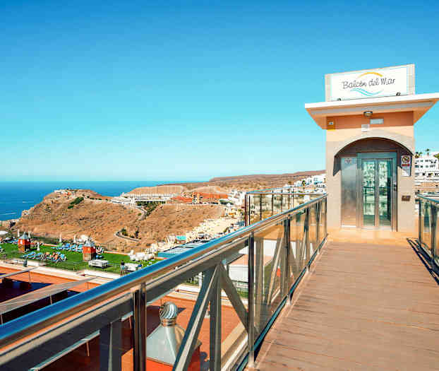 En glas-elevator ved en gangbro med udsigt over et landskab og havet. (AI-genereret tekst)