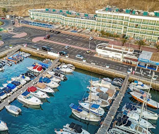 Luftfoto af en marina med parkerede både foran bygninger og parkeringsplads. (AI-genereret tekst)