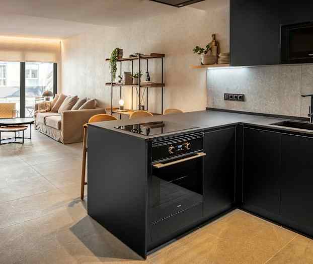 Billede af en moderne stue og køkken med stilfuld indretning. Viser en grå køkkenø og en sofa i baggrunden. (AI-genereret tekst)