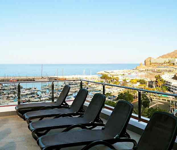 Billede af en terrasse med liggestole med udsigt over en marina og havet. (AI-genereret tekst)