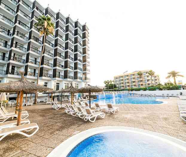 Billede af et hotelområde med pool, liggestole og parasoller. (AI-genereret tekst)