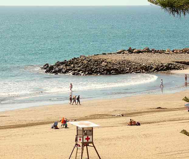 Strand med badegæster, livreddertårn og klipper ved havet. (AI-genereret tekst)