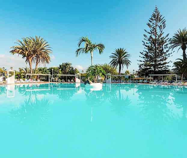 En stor turkis swimmingpool omgivet af liggestole og palmer. (AI-genereret tekst)