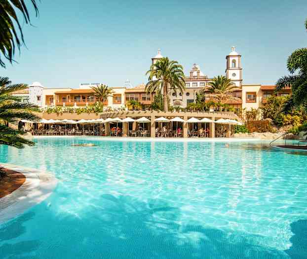 En stor pool foran en bygning med palmer og parasoller. (AI-genereret tekst)