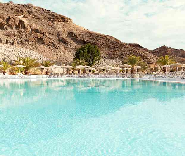 Stor pool med solsenge og parasoller ved foden af bjerge. (AI-genereret tekst)