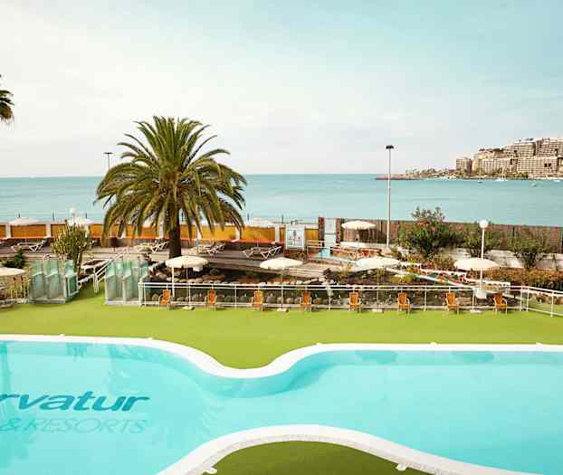 En pool med udsigt over havet og en solrig terrasse med liggestole. (AI-genereret tekst)