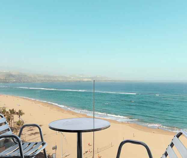 Udsigt fra en balkon mod en sandstrand og havet. (AI-genereret tekst)