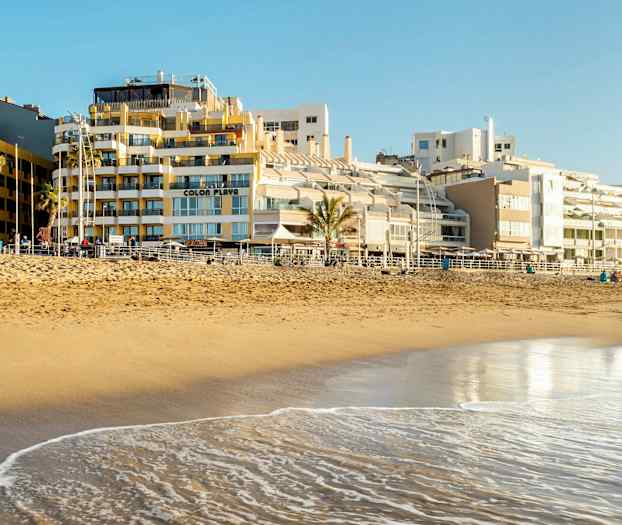 En sandstrand ved havet med bygninger i baggrunden. (AI-genereret tekst)