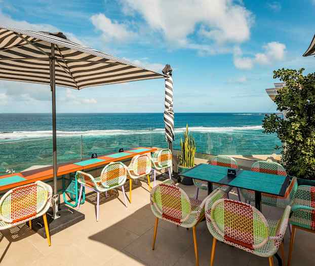 Udendørs serveringsområde med farverige stole og udsigt over havet. (AI-genereret tekst)