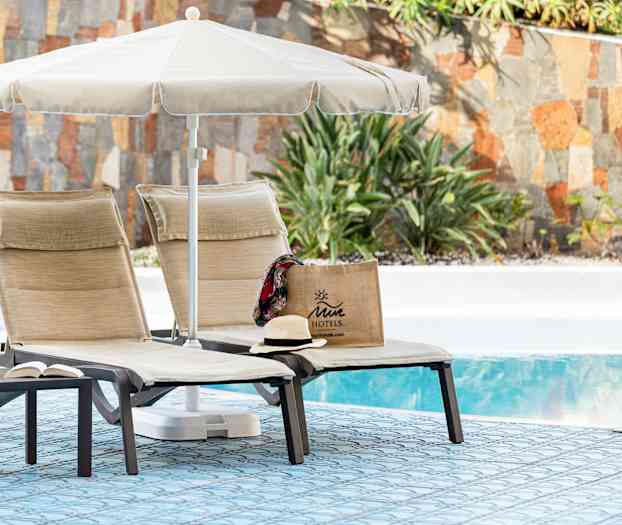 To liggestole med parasol ved en pool, med en Juicy motel taske og en hat. (AI-genereret tekst)