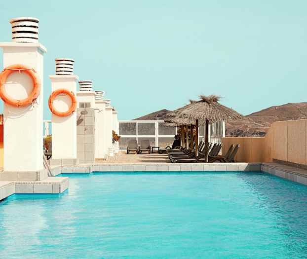 Udendørs pool med solsenge og parasoller ved siden af. (AI-genereret tekst)