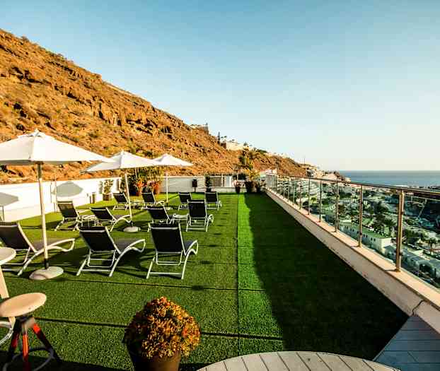 Billede af en terrasse med liggestole, parasoller og udsigt over havet og omkringliggende klipper. (AI-genereret tekst)