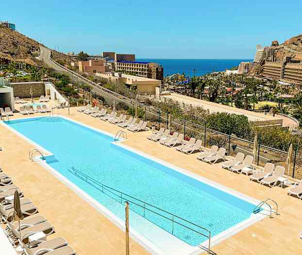 En udendørs pool omgivet af liggestole med havudsigt i baggrunden. (AI-genereret tekst)