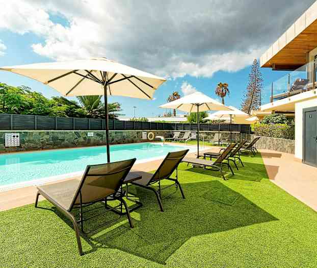 En udendørs pool med liggestole og parasoller på græs og terrasse. (AI-genereret tekst)
