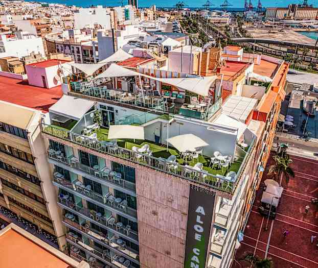 En bygning med terrasser på toppen, omgivet af en by med havet i baggrunden. (AI-genereret tekst)