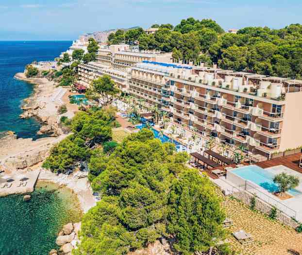 Fleretagers hotel ved kysten med en swimmingpool foran og omkringliggende beplantning. (AI-genereret tekst)