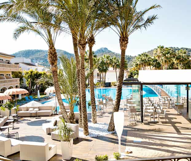 Et poolområde med liggestole, parasoller, palmer og en bygning i baggrunden. (AI-genereret tekst)