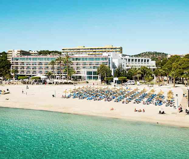 En strand med parasoller og liggestole foran en stor bygning med altaner. (AI-genereret tekst)