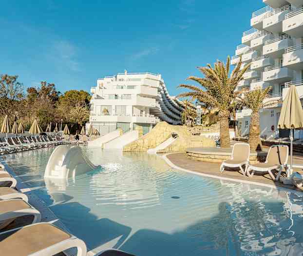 Poolområde med liggestole og parasoller ved hotelbygning. (AI-genereret tekst)