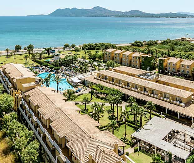 Luftfoto af en feriekompleks ved havet med pool, grønne områder og flerboligbygninger. (AI-genereret tekst)