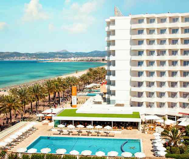 Hotel ved stranden med pool og liggestole, hav i baggrunden. (AI-genereret tekst)