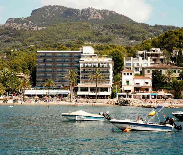 Et billede af en kystby med hotel, strand og både ved vandet. (AI-genereret tekst)