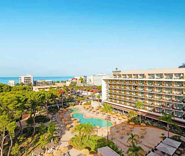 Udsigt over hotelområde med pool, grønne områder og hav i baggrunden. (AI-genereret tekst)