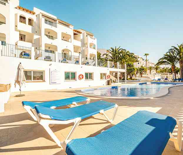 Udendørs swimmingpool med liggestole og hvide bygninger i baggrunden. (AI-genereret tekst)