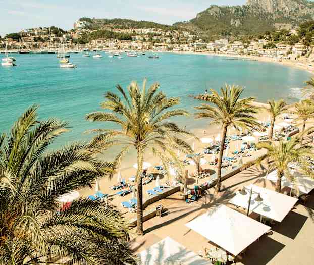 Strand med palmer og liggestole. Smuk udsigt over havet og nærliggende bygninger. (AI-genereret tekst)