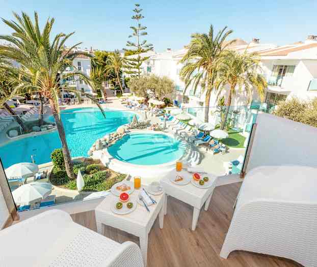 Udsigt fra terrasse mod poolområde med liggestole, palmer og morgenmadsbord. (AI-genereret tekst)