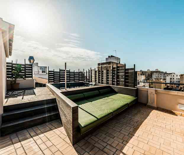 En tagterrasse med en grøn siddeplads og udsigt over de omkringliggende bygninger. (AI-genereret tekst)