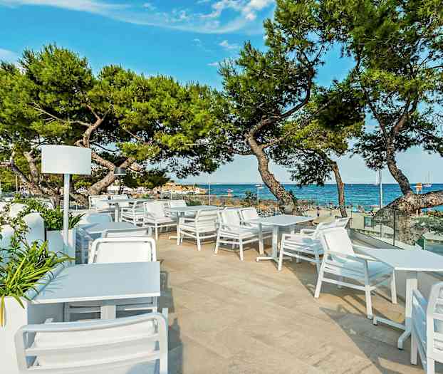 Udendørs servering med hvide møbler og udsigt over havet og stranden. (AI-genereret tekst)