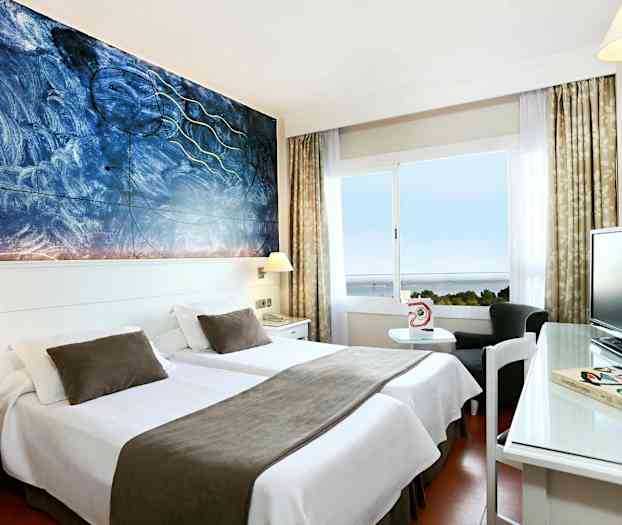 Et hotelværelse med to enkeltsenge med hvidt sengetøj og brune sengetæpper, et kunstnerisk maleri på væggen og et vindue med udsigt over havet. (AI-genereret tekst)